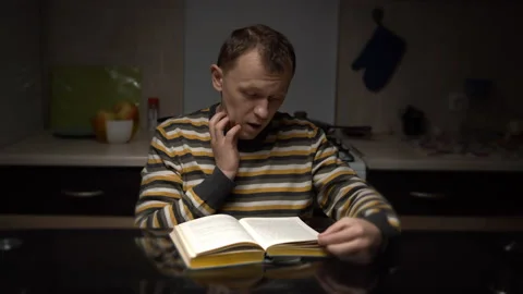 Young man student with expression reads text from a book while sitting Stock Footage 130928224