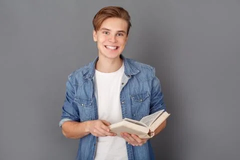 Young man student in jeans jacket studio isolated on grey reading book joyful Stock Photos