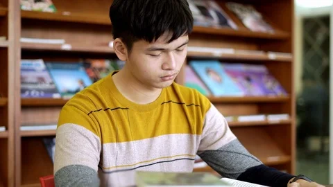 Young man student in library desk reading and yawning tired In the afternoon  Stock Footage 122586232