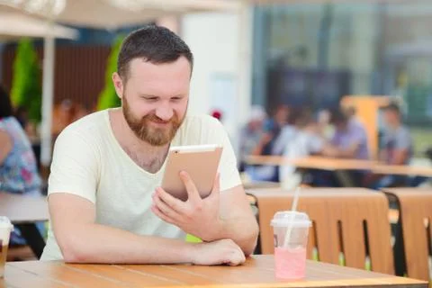 Young man student using a tablet computer in a cafe with a cool drink in the  Stock Photos