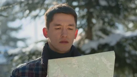 A young man studies a map while standing in a snowy forest. A man lost in a Stock Footage 237033800