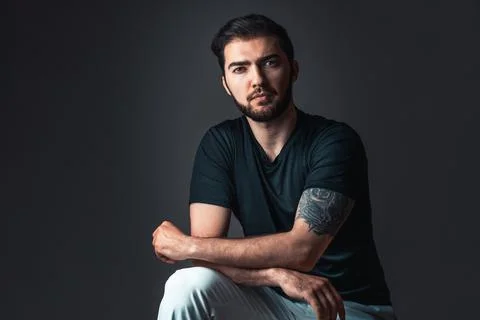Young man in studio on dark background. Handsome brunette with beard and tatt Stock-Fotos