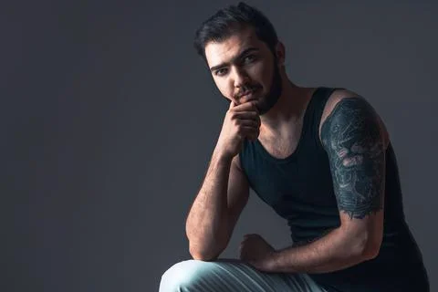 Young man in studio on dark background. Handsome brunette with beard and tatt Stock Photos