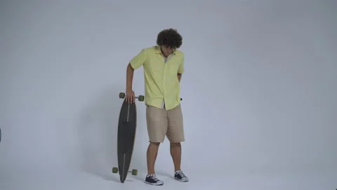 Young man in the studio leans on a longboard. Curly guy stands with a longboard Video stock 139856239