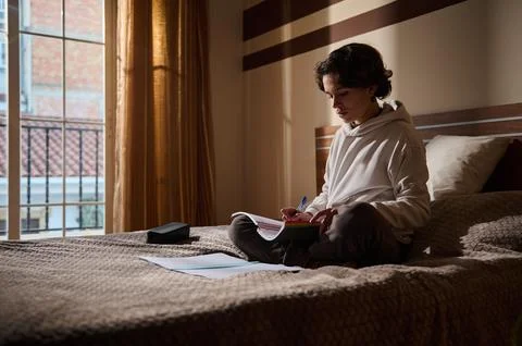 Young Man Studying on Bed by Window With Notebook and Pens Stock-Fotos