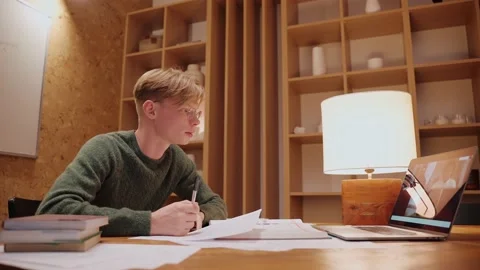 Young man studying at home, having a video call on a laptop, writing his notes Video stock 164380698