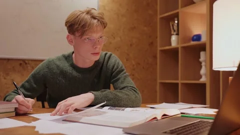 Young man studying at home looking at the laptop, writing in a notebook Video stock 164380508