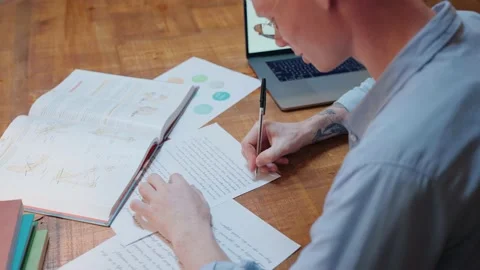 Young man studying at home writes in his notes and reads a textbook Vídeo Stock 164374270