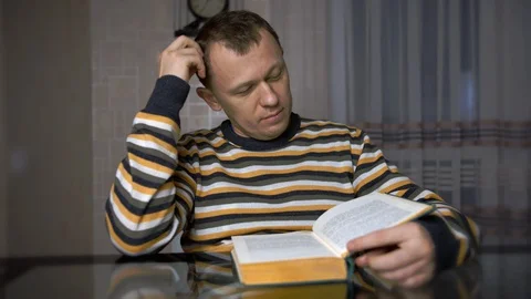 A young man is studying text in a green paper while sitting at a table. Stock Footage 128869746