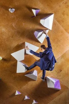 Young man in suit climbing difficult route on artificial wall Stock Photos