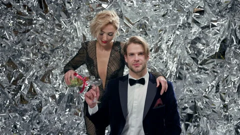 Young Man In Suit Sitting On Silver Background. Girl In An Evening Dress Pours Stock Footage 179073505
