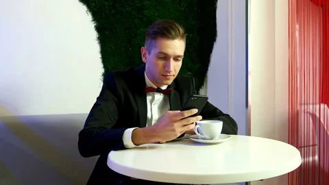 Young man in a suit sitting at table and using smartphone in a cafe Stock Footage 75809057