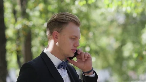 Young man in a suit talking on the phone in the park Stockbeeldmateriaal 81386403