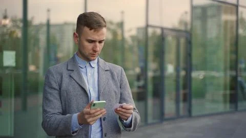 Young man in suit using information from visit card and smartphone. Slow motion Foto stock