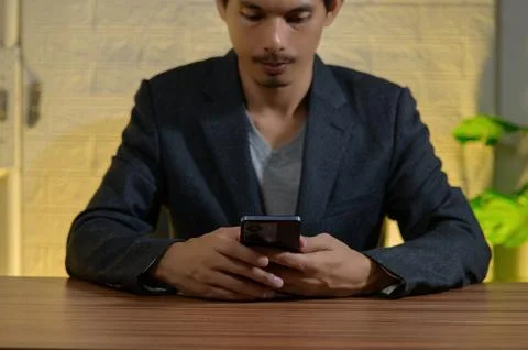 Young man in suit using smartphone at wooden table indoors Stock Photos