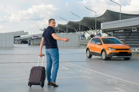 A young man with a suitcase and with a remote car key in an open parking lot. Stock Photos