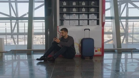 A young man with a suitcase sits on the floor near the phone charging station. Stock Footage 123539769