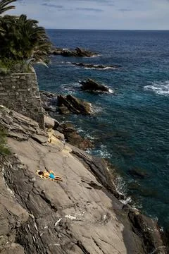 Young man sunbathing on the slope of a cliff by the sea on a sunny day Stock Photos