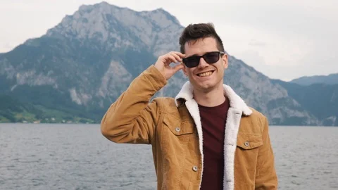 A young man in sunglasses against the background of a lake and a mountain in Stock Footage 129784372