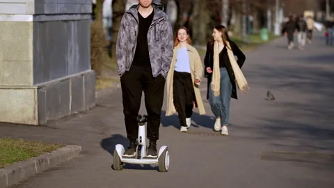 A young man in sunglasses is having fun riding a hoverboard in early spring on a Stock Footage 152301484