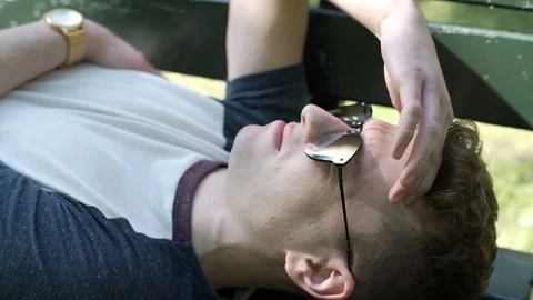 Young man in sunglasses lying on the bench and having a headache, steadycam shot Stock-Footage 76384899