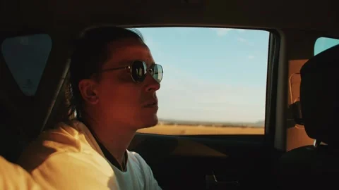 Young man in sunglasses sits in back seat of car and carefully looks ahead Vídeo Stock 247330744