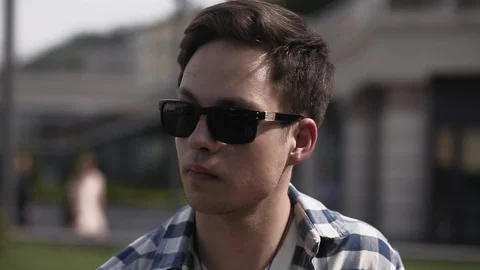 A young man with sunglasses is sitting on the background of the city and is Video stock 130132216