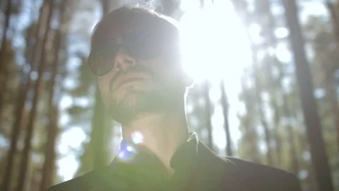 Young man in the sunglasses standing in the forest and is backlit by the sun Stock Footage 83223464