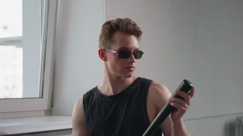 Young man in sunglasses taps baton on hand with grin Stock Footage 308658682
