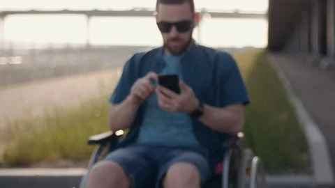 Young man in sunglasses using mobile phone, physically disabled man sits in Stock Footage 110211212