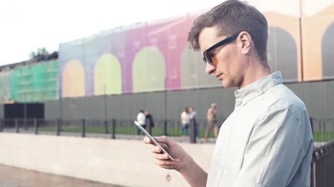 Young man in sunglasses using smartphone standing at city park Stock Footage 79357270