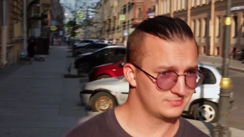 Young man in sunglasses walks down city street on sunny day Stock Footage 204883720