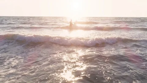 Young man surfer wearing wetsuit carrying surf board walking in the calm ocean 스톡 동영상 85437360
