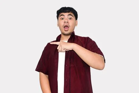 Young man with surprised expression pointing finger on plain background, As.. Stock Photos