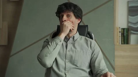 Young man with a surprised expression is sitting in a chair in the office 스톡 동영상 154717245