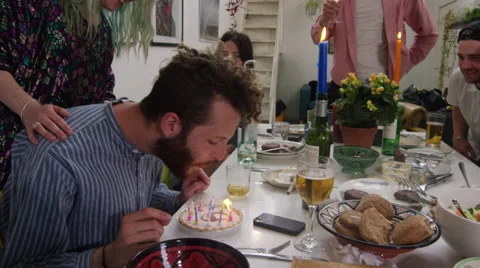 Young man surrounded by friends blowing out candles on cake at dinner party Stock Footage 58581925