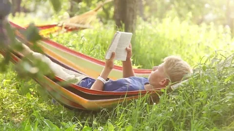 Young man sways lying in the hammock and reads a book during siesta Stock-Footage 69165646