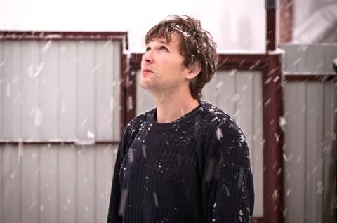 Young man in sweater looking up on falling snowflakes outdoor winter season s Stock Photos