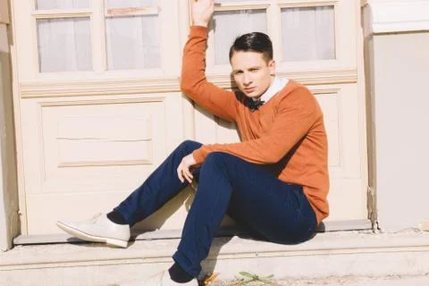 Young man in sweater sitting on steps in front of house and posing Stock Photos