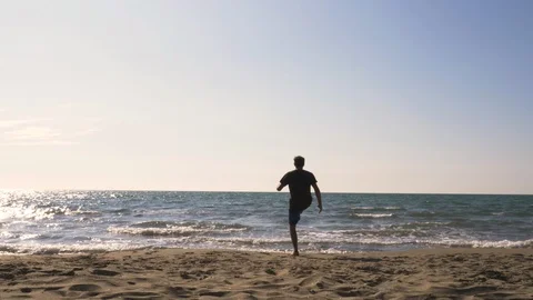 Young man in swimming trunks does tricks dribbling bouncing football on the sea Stock Footage 108696669