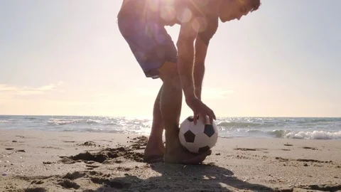 Young man in swimming trunks doing tricks holding football on the foot on the Stock Footage 84996383