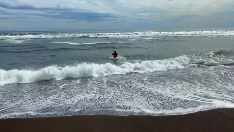 A young man swims on the beach with black volcanic sand Stock Footage 141246953