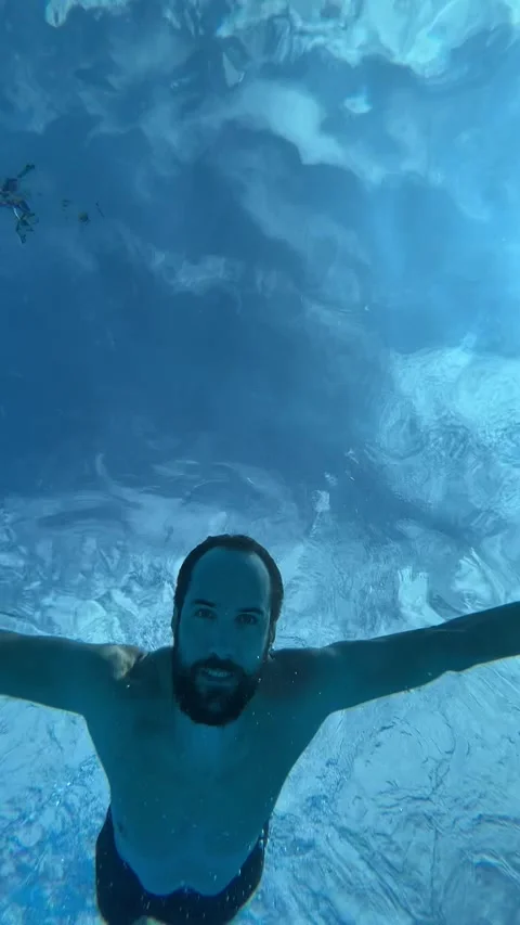 A young man swims in a blue pool and dives underwater Stock Footage 237761837
