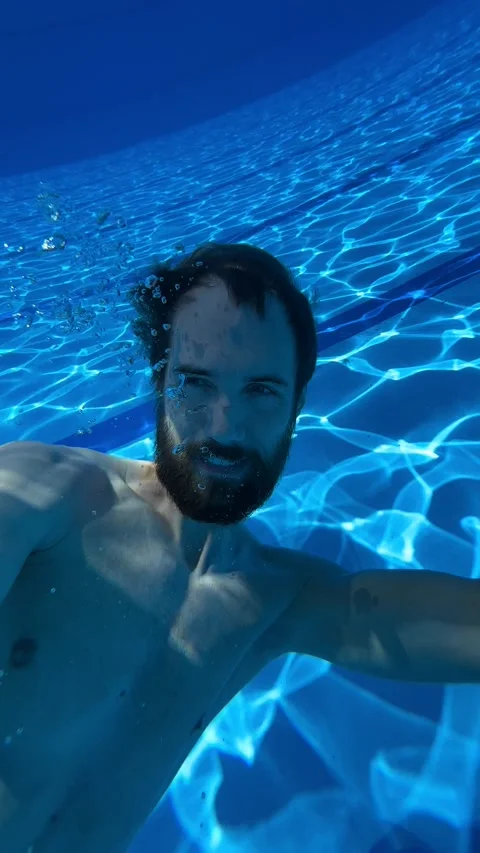 A young man swims in a blue pool and dives underwater Stock Footage 237761852