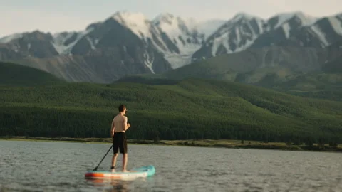 A young man swims on a SUP board in a mountain lake. Stock Footage 281160153