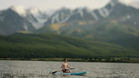 A young man swims on a SUP board in a mountain lake. Stock Footage 281262406
