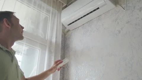 Young man switching on air conditioner at home for comfort temperature with Stock Footage 244847576