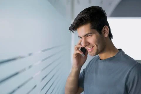 Young man in T-shirt using mobile phone in glass office Stock Photos