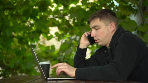 A young man at a table in a gazebo talks on the phone during the day. A man in a Stock Footage 251726850
