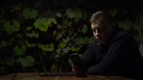 A young man at a table in a gazebo is texting on a smartphone late at night. A Stock Footage 251830931